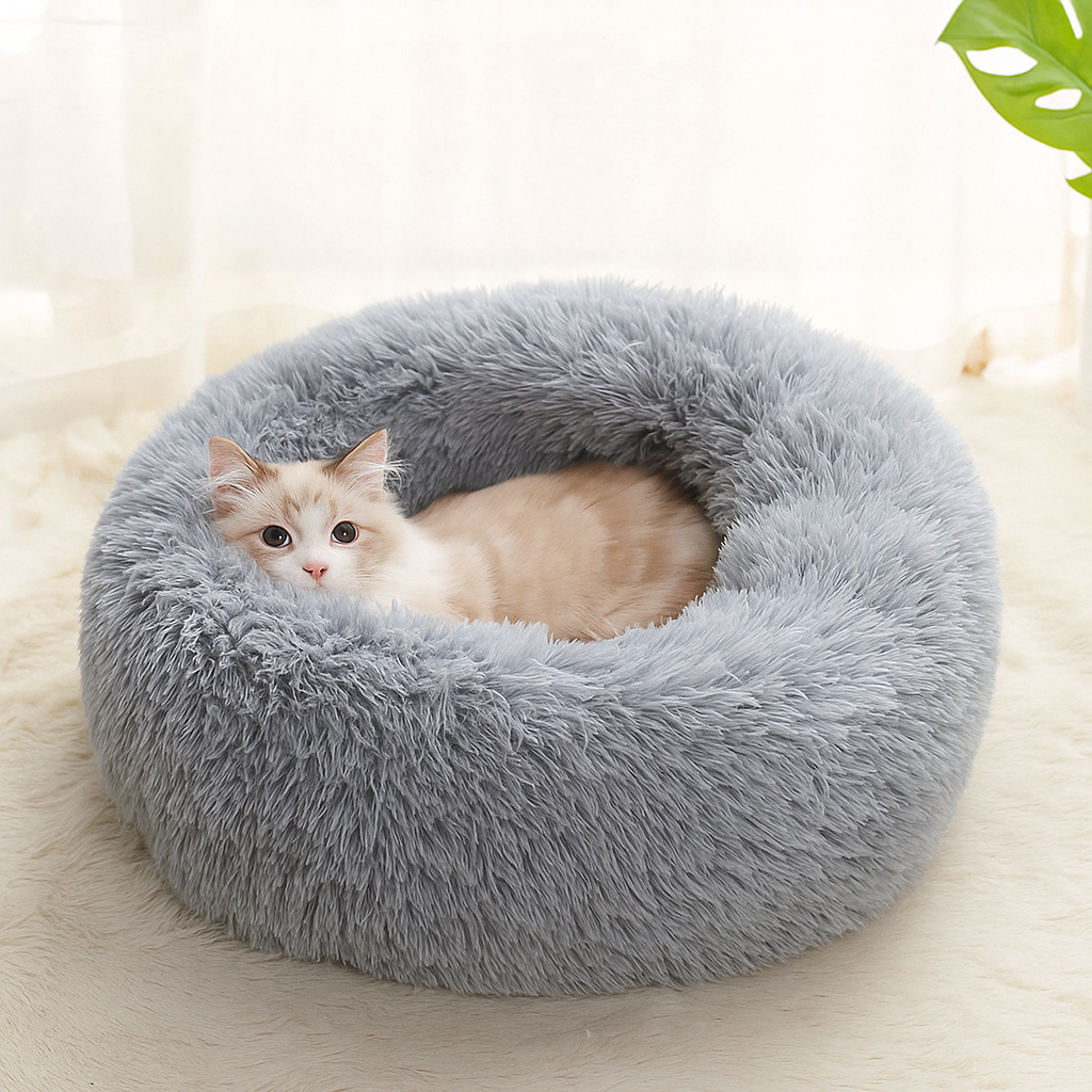 Cat lying in a fluffy gray pet bed on a light wooden floor.